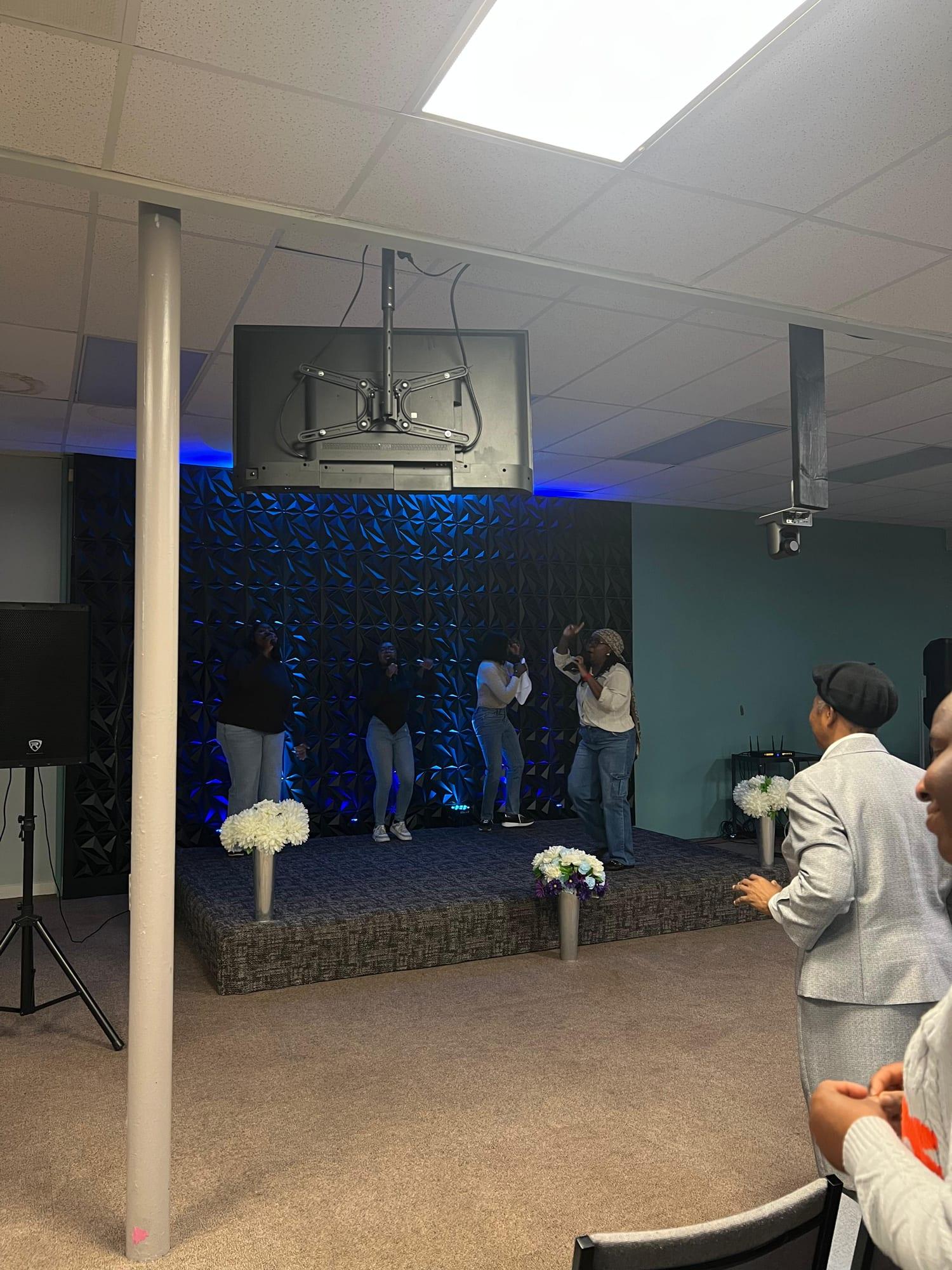 The room from the back: singers on the stage and people standing in worship in the foreground.