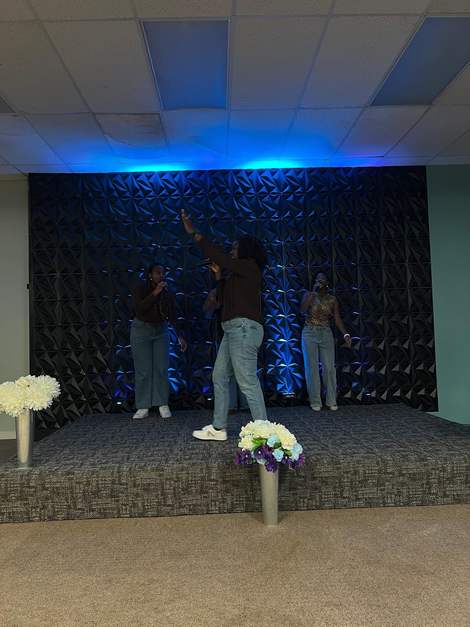 A worship leader in motion with one hand raised, two singers on either side of her.