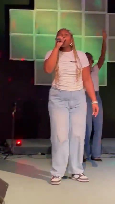 Video: a singer in a white top leads with her hand lifted high.